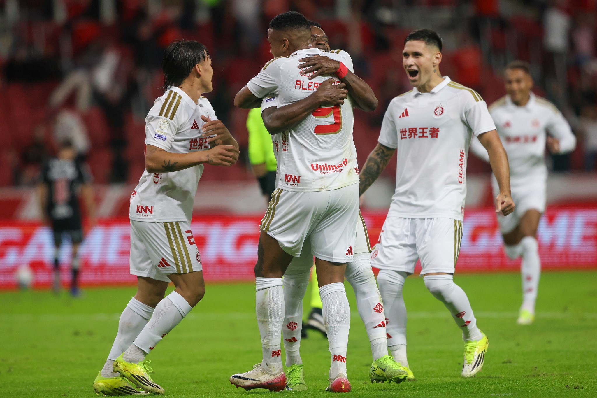 Jogadores do Internacional Alerrandro, Bernabei e Carbonero comemoram gol contra o Vasco no Beira-Rio, vestindo o novo uniforme branco e dourado.