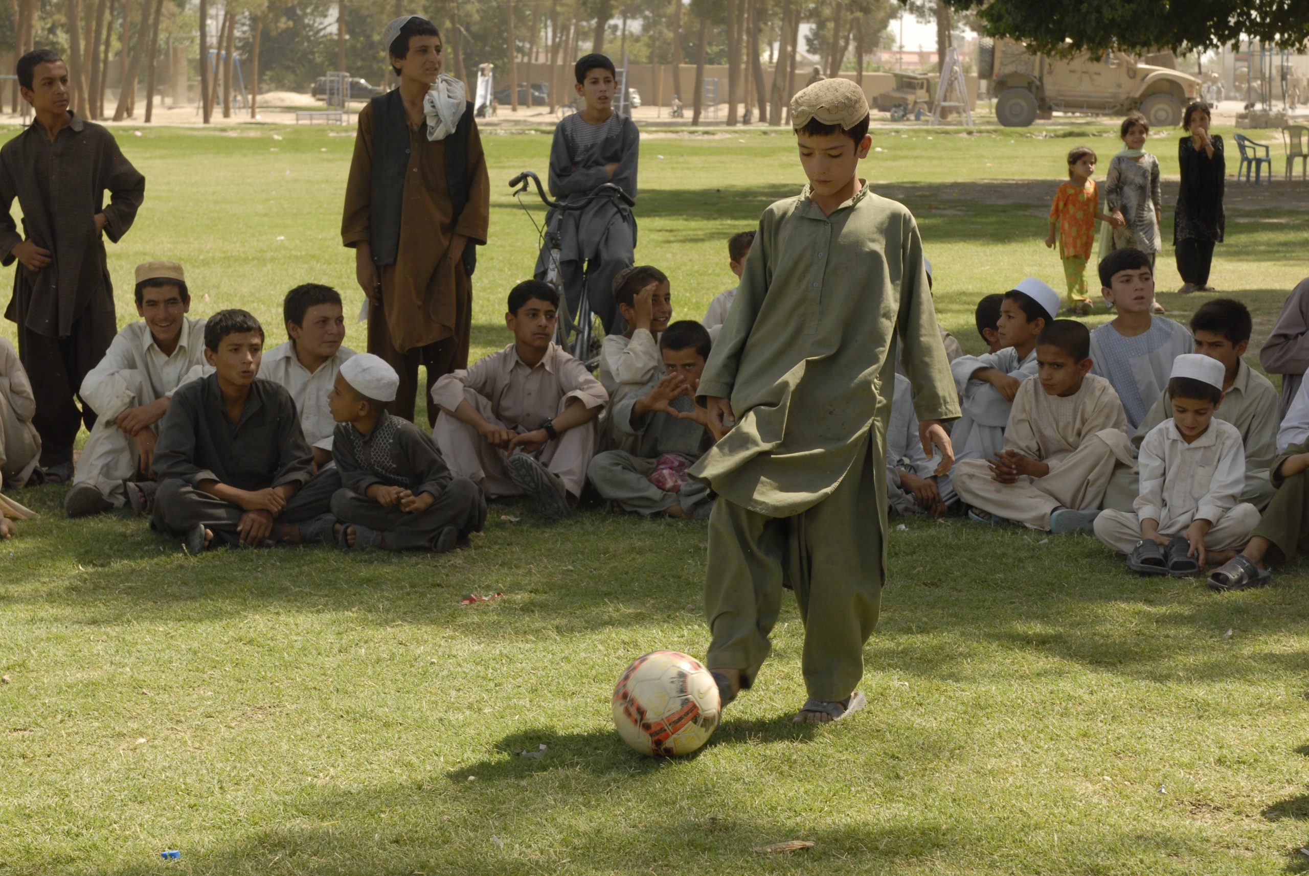 Bola de futebol branca e preta rolando em campo de grama natural sob luz do sol
