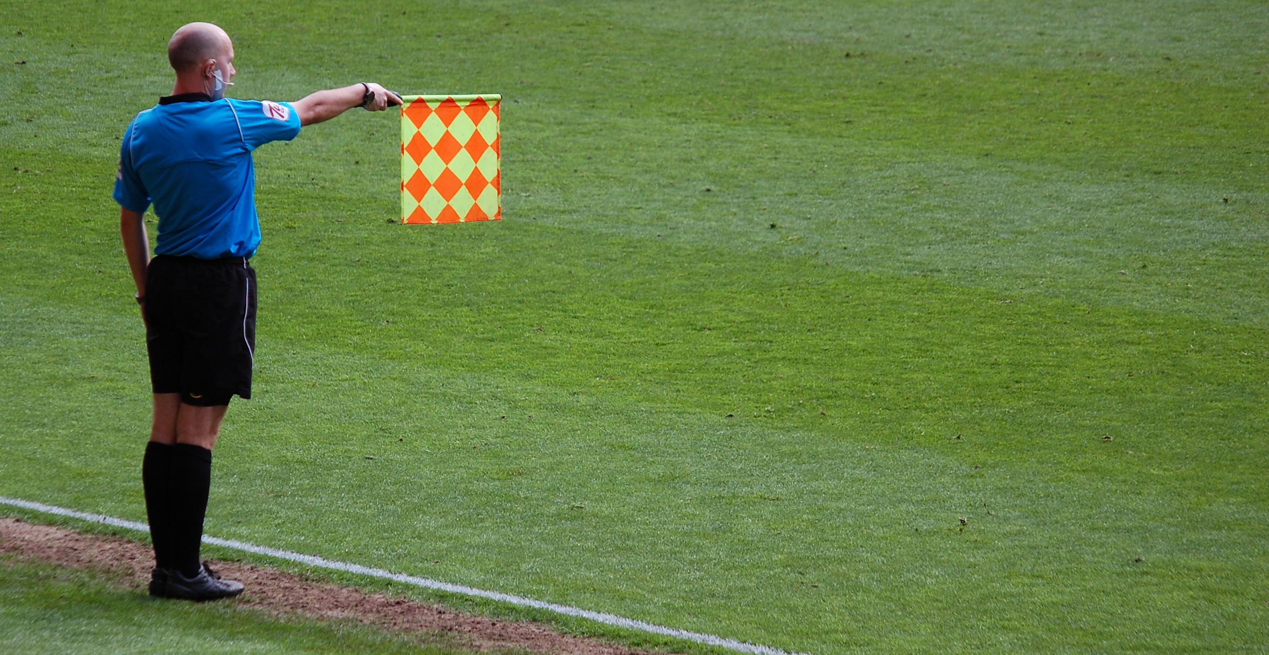 Um jogador de futebol em posição de impedimento durante uma partida, com a linha de defesa adversária ao fundo.