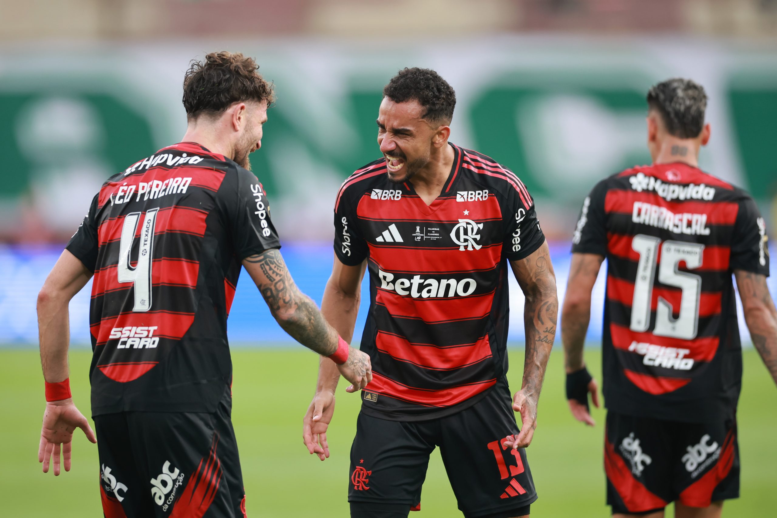 Jogadores do Flamengo em ação durante uma partida, com destaque para a camisa rubro-negra e o escudo do clube.