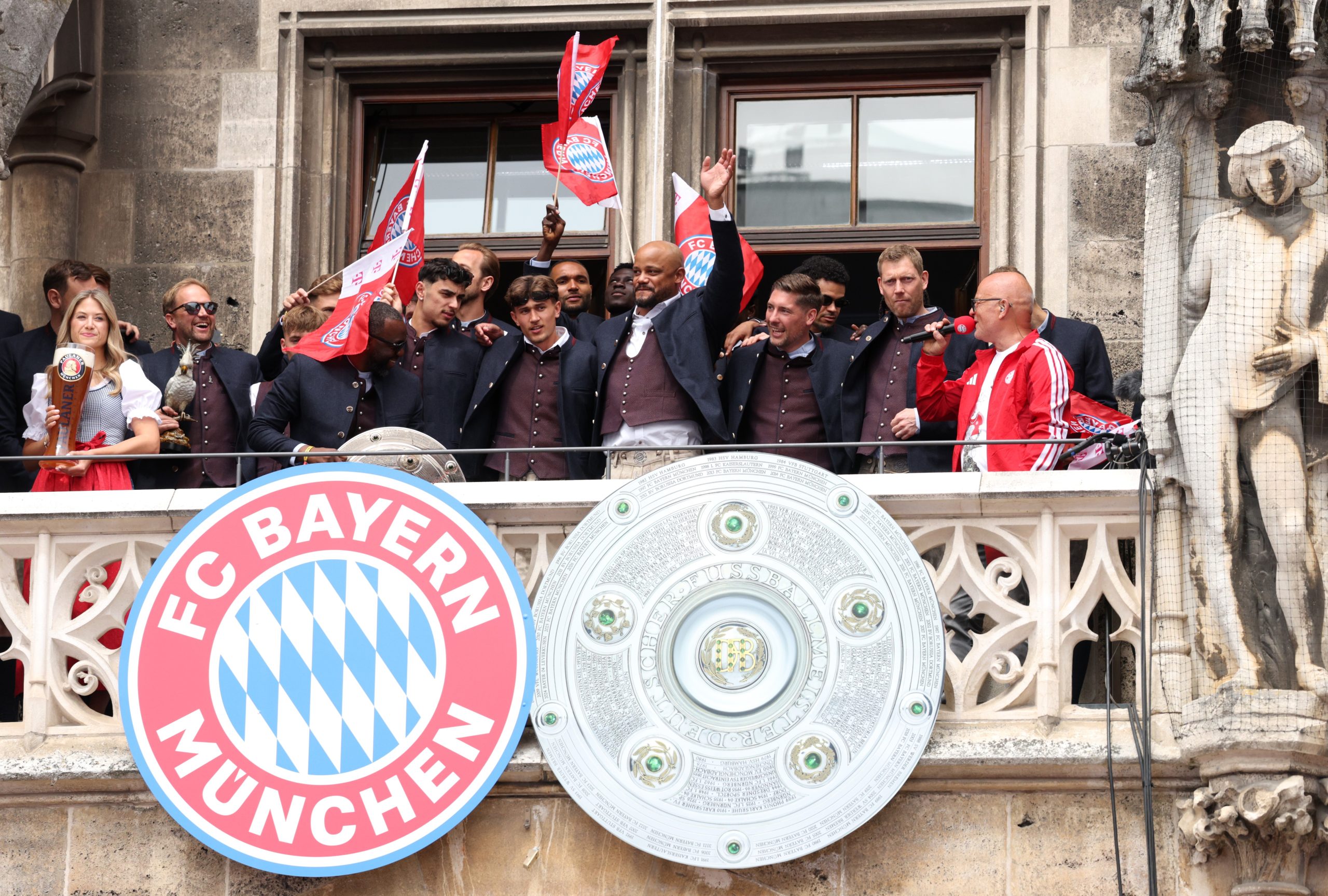 Jogadores do Bayern de Munique comemoram o título da Bundesliga na varanda de um prédio, com a Marienplatz lotada de torcedores.