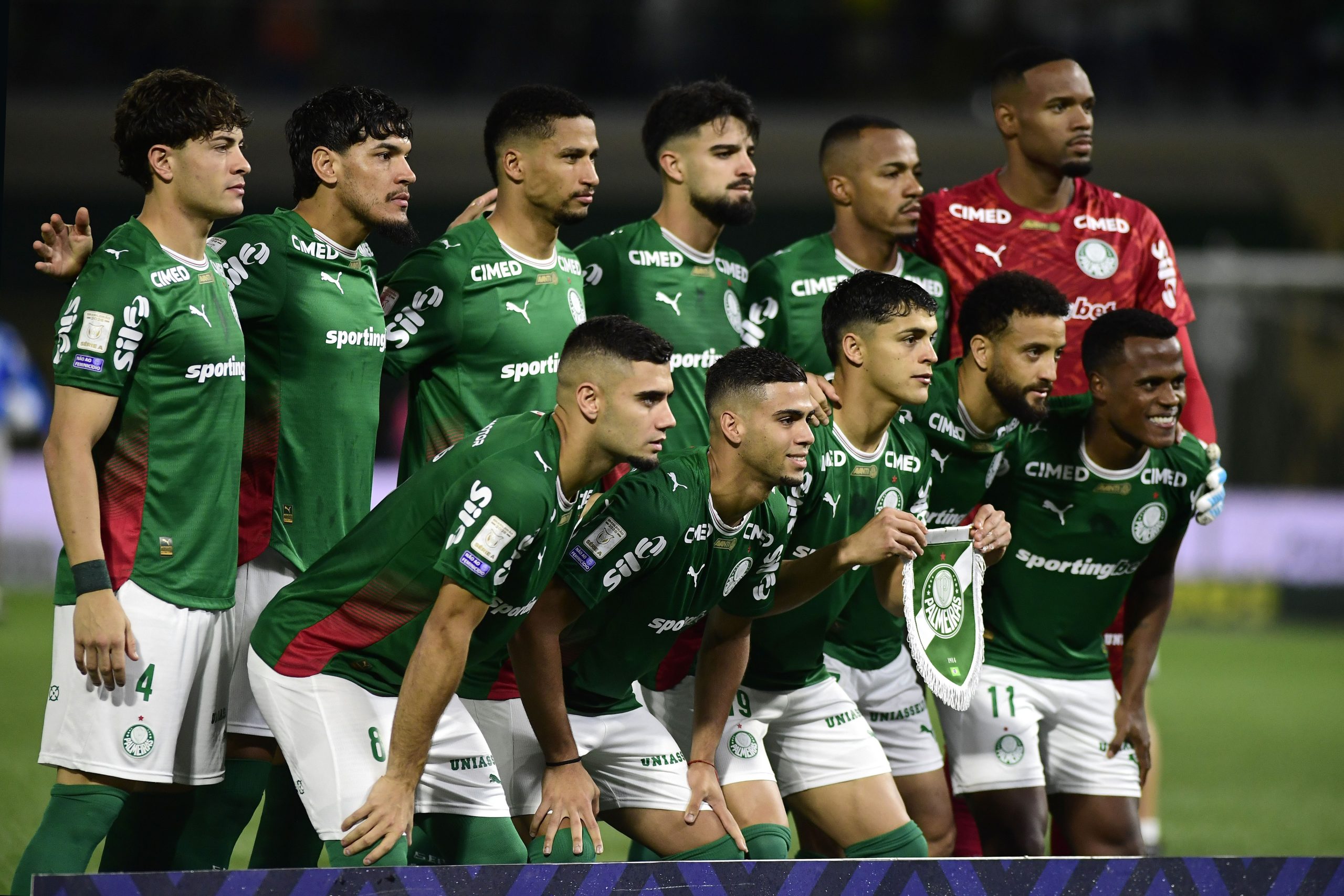 Jogadores do Palmeiras em campo, em momento de jogo crucial, com a torcida ao fundo
