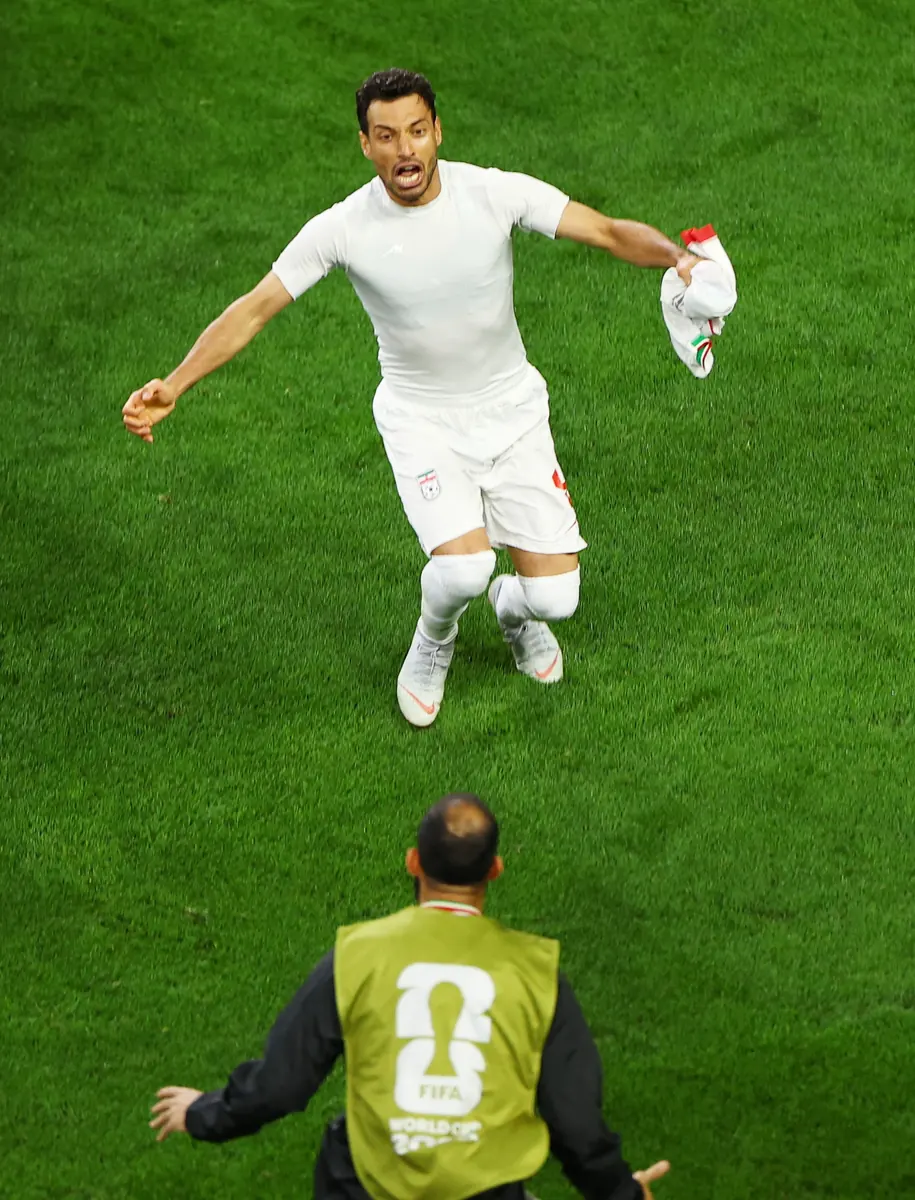 Jogador da seleção do Irã comemora um gol em partida da Copa do Mundo, com a imagem do VAR em destaque.
