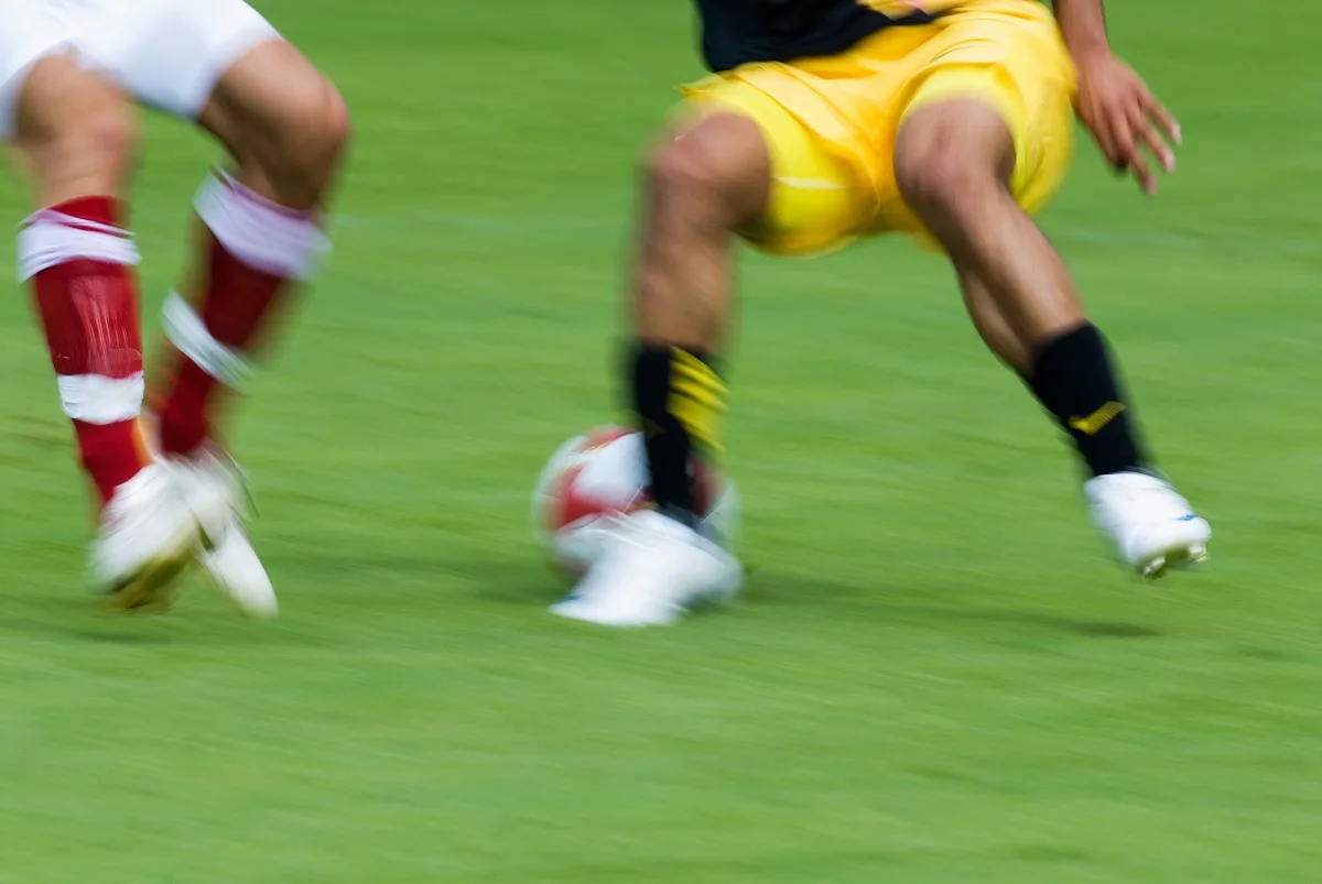 Jogadores de futebol em campo com bola e logo da Copa do Mundo ao fundo