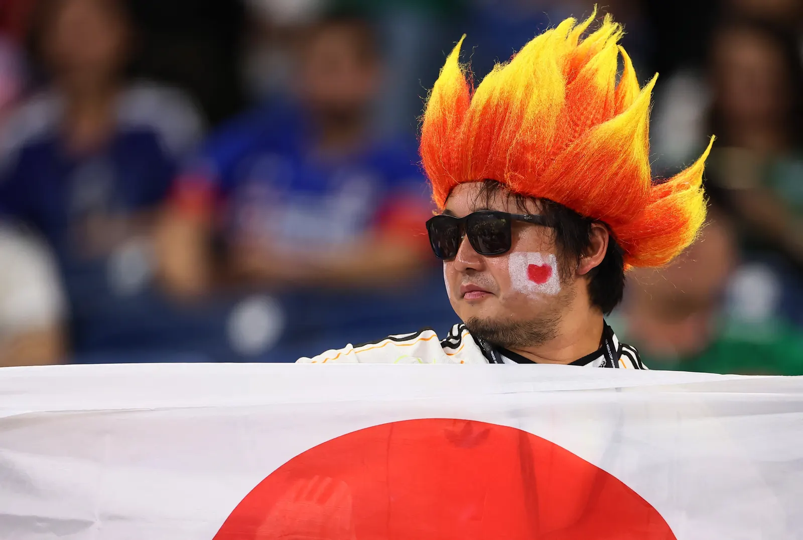 Torcedores japoneses com maquiagens e fantasias vibrantes exibindo apoio à seleção em um estádio de futebol.