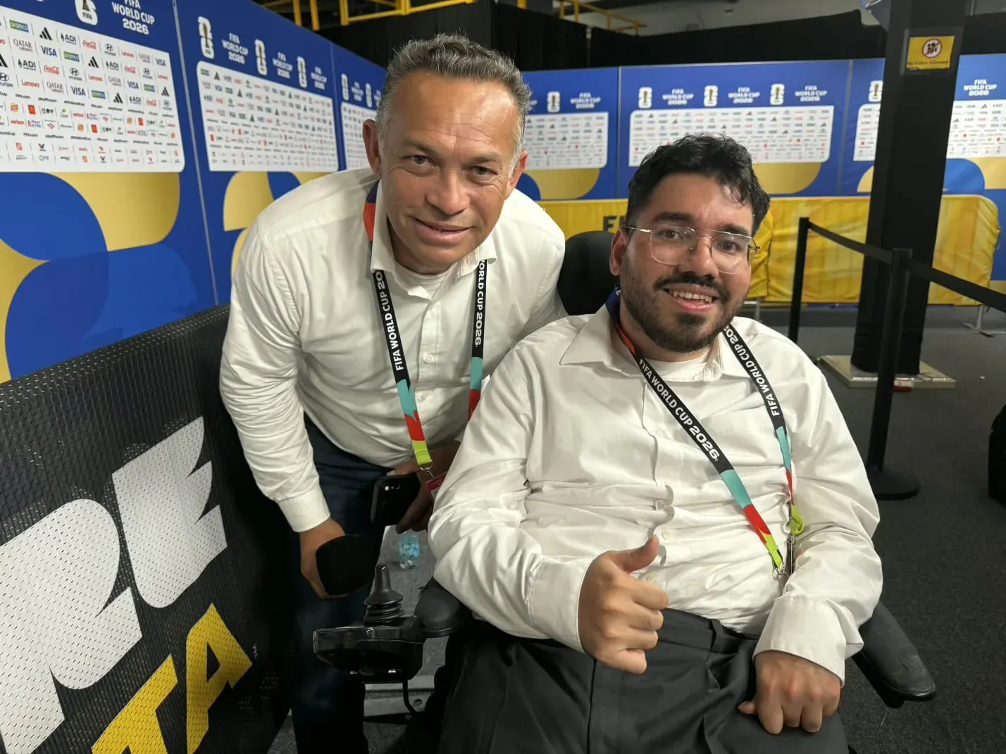 Jornalista Manu Gutiérrez em sua cadeira de rodas, sorrindo enquanto entrevista um jogador de futebol durante a Copa do Mundo.