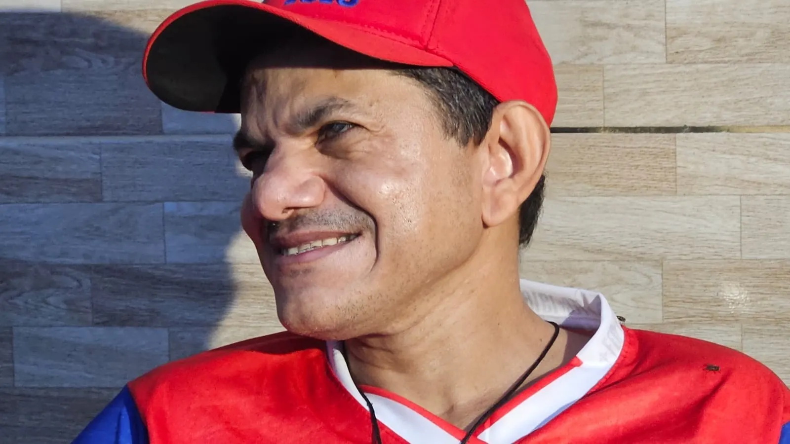 Manoel Gomes, torcedor cego do Fortaleza, sentado na calçada de casa com a bandeira do clube ao fundo